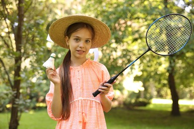 Photo of Portrait of smiling little girl in hat with badminton racket and shuttlecock in park