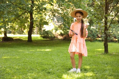 Photo of Smiling little girl in hat and dress with badminton racket and shuttlecock in park. Space for text