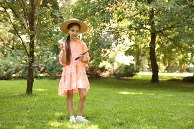 Photo of Smiling little girl in hat and dress with badminton racket and shuttlecock in park