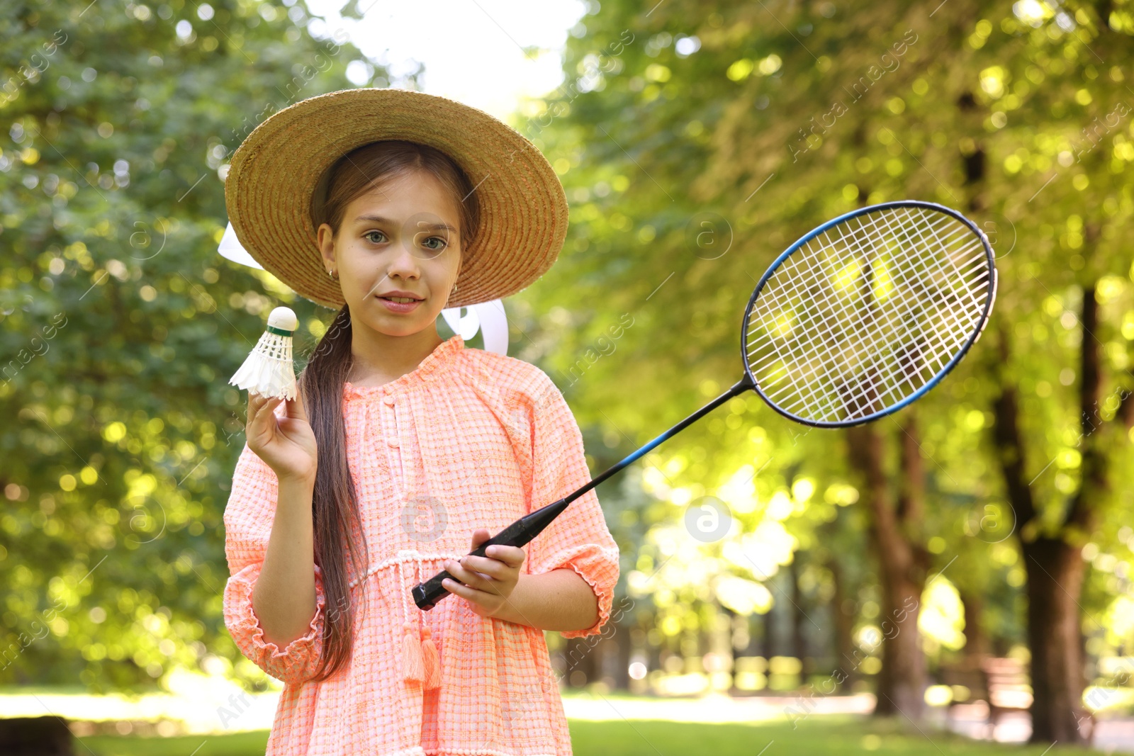 Portrait of smiling little girl in hat with badminton racket and shuttlecock in park Photo of Portrait of smiling little girl in hat with badminton racket and shuttlecock in park