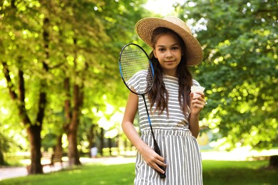 Photo of Cute little girl in hat with badminton racket and shuttlecock in park. Space for text