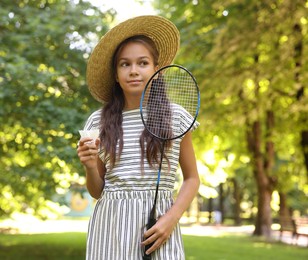 Photo of Cute little girl in hat with badminton racket and shuttlecock in park