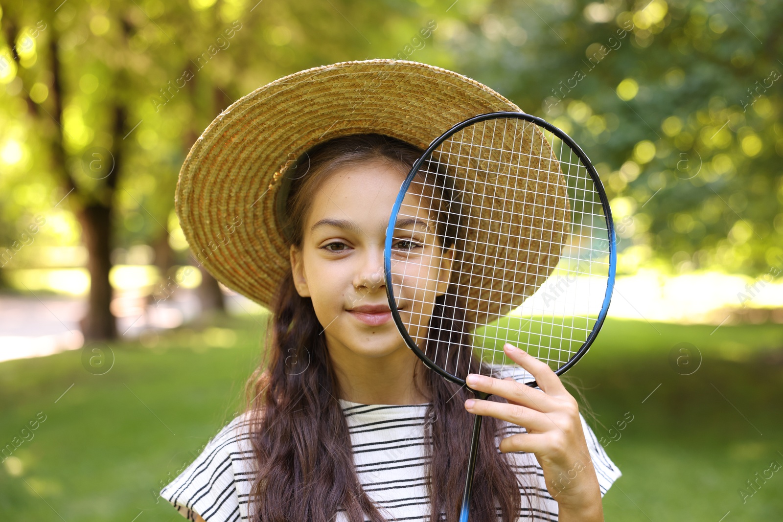 Smiling little girl in hat with badminton racket in park Photo of Smiling little girl in hat with badminton racket in park