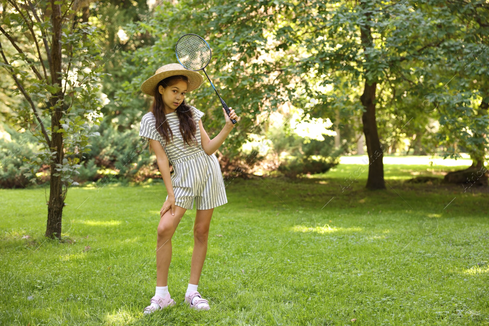 Cute little girl in hat with badminton racket in park. Space for text Photo of Cute little girl in hat with badminton racket in park. Space for text