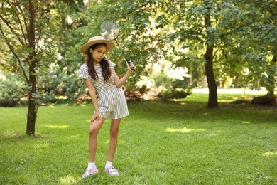 Photo of Cute little girl in hat with badminton racket in park. Space for text