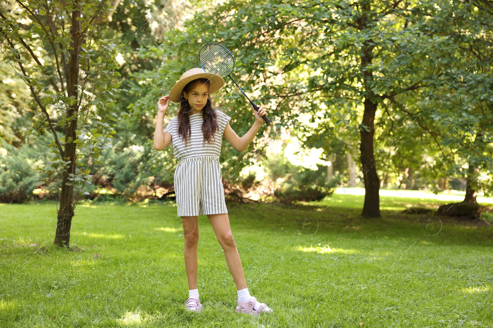 Cute little girl in hat with badminton racket in park. Space for text Photo of Cute little girl in hat with badminton racket in park. Space for text