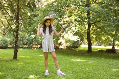 Photo of Cute little girl in hat with badminton racket in park. Space for text