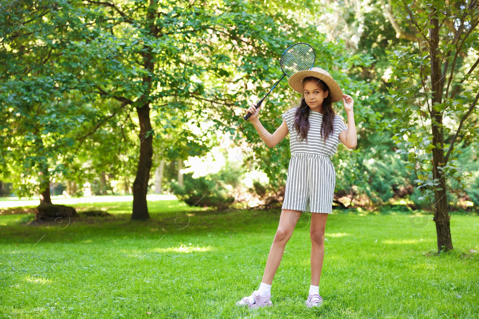 Cute little girl in hat with badminton racket in park. Space for text Photo of Cute little girl in hat with badminton racket in park. Space for text
