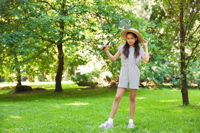 Photo of Cute little girl in hat with badminton racket in park. Space for text
