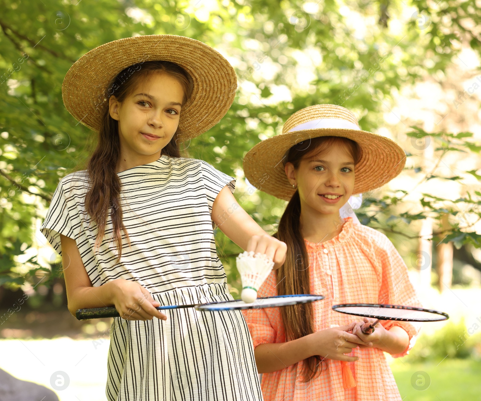 Portrait of smiling little girls in hats with badminton rackets and shuttlecock in park Photo of Portrait of smiling little girls in hats with badminton rackets and shuttlecock in park