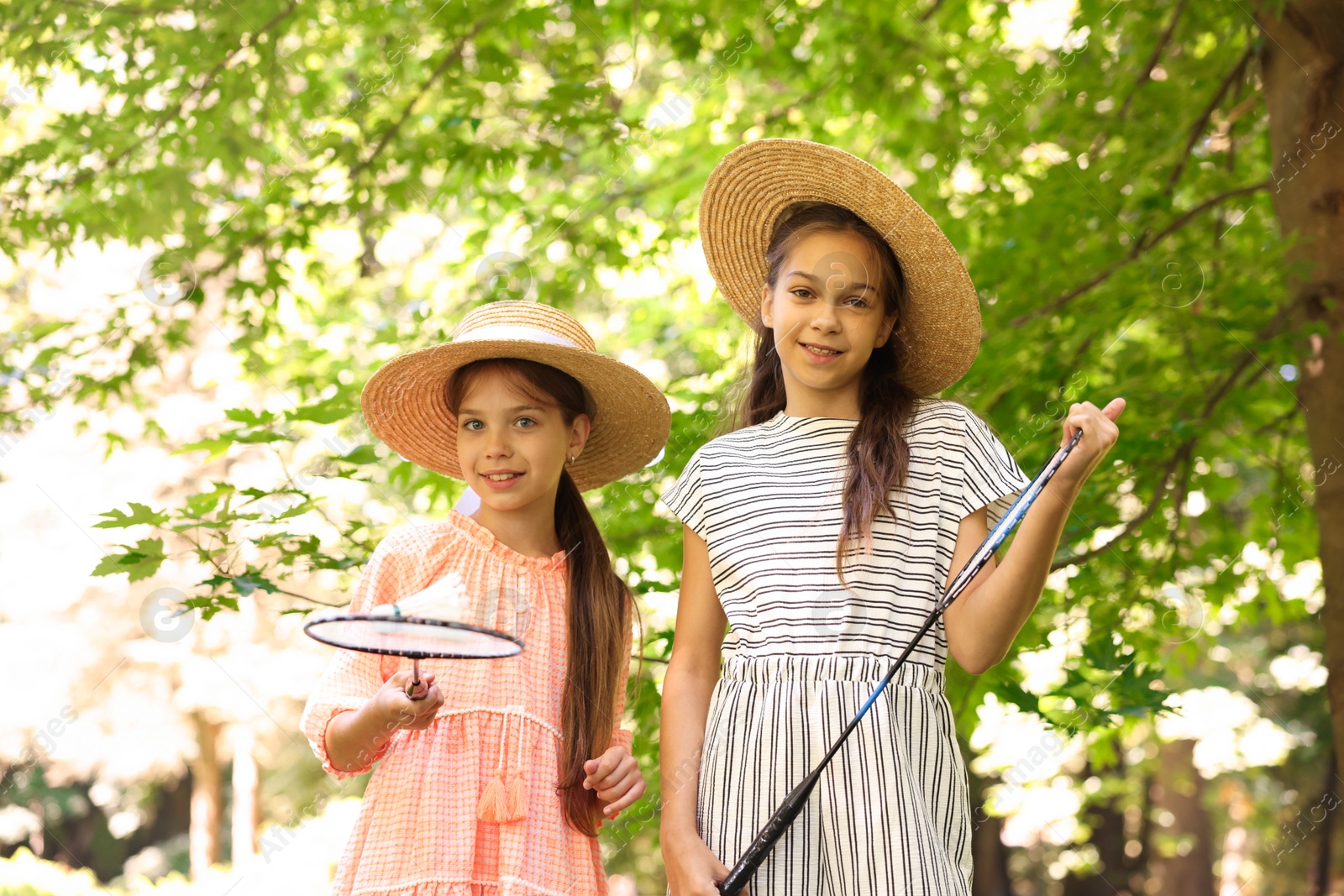 Portrait of smiling little girls in hats with badminton rackets and shuttlecock in park, low angle view Photo of Portrait of smiling little girls in hats with badminton rackets and shuttlecock in park, low angle view