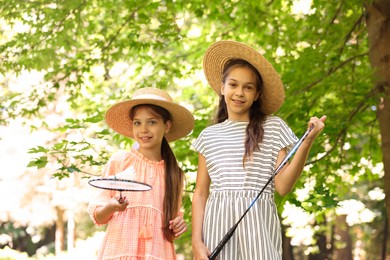 Photo of Portrait of smiling little girls in hats with badminton rackets and shuttlecock in park, low angle view