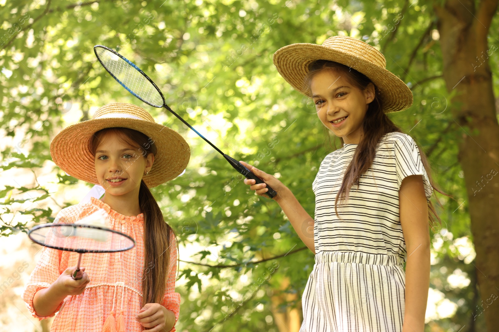 Portrait of smiling little girls in hats with badminton rackets and shuttlecock in park, low angle view Photo of Portrait of smiling little girls in hats with badminton rackets and shuttlecock in park, low angle view
