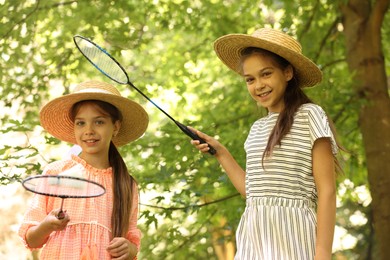Photo of Portrait of smiling little girls in hats with badminton rackets and shuttlecock in park, low angle view