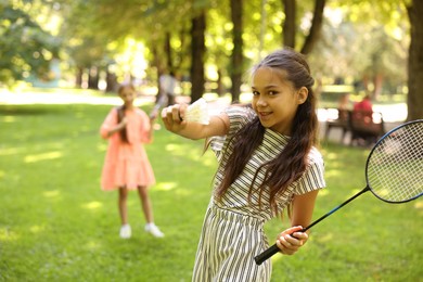 Photo of Smiling little girl with badminton racket and shuttlecock playing with her friend in park, selective focus