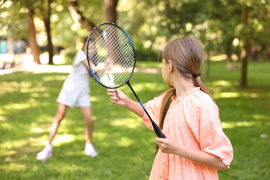 Photo of Little girl with badminton racket and shuttlecock playing with her friend in park, selective focus