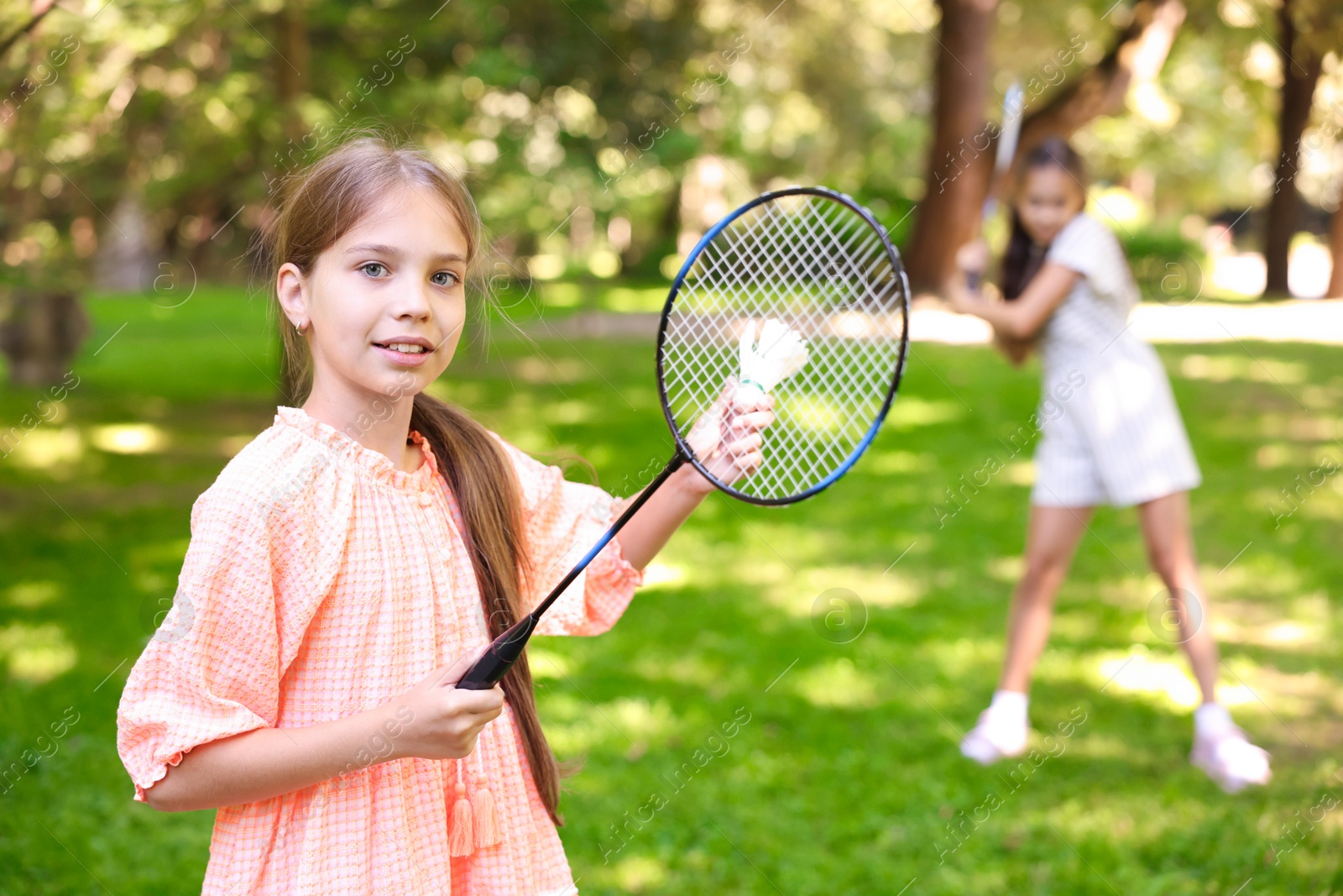 Smiling little girl with badminton racket and shuttlecock playing with her friend in park, selective focus Photo of Smiling little girl with badminton racket and shuttlecock playing with her friend in park, selective focus