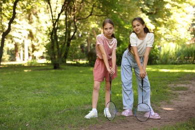 Photo of Cute little girls with badminton rackets posing in park. Space for text