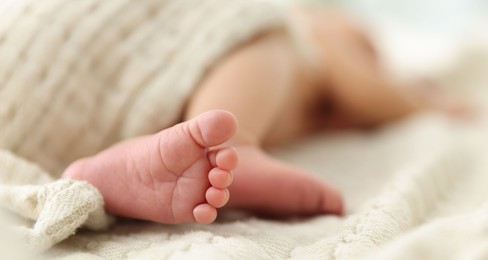 Photo of Cute newborn baby lying on bed indoors, closeup. Space for text