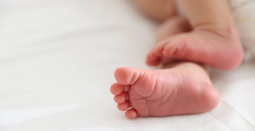 Photo of Cute newborn baby lying on bed indoors, closeup. Space for text