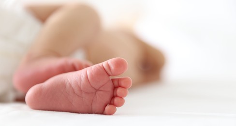 Photo of Cute newborn baby lying on bed indoors, closeup. Space for text