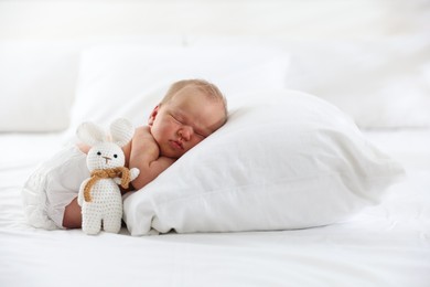 Photo of Cute newborn baby sleeping on pillow and toy bunny indoors