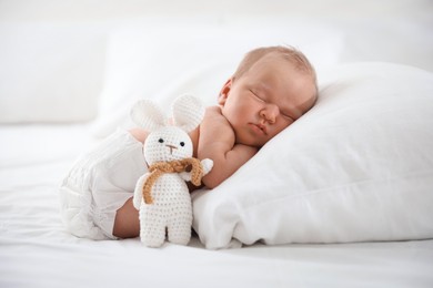 Photo of Cute newborn baby sleeping on pillow and toy bunny indoors