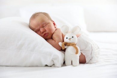 Photo of Cute newborn baby sleeping on pillow and toy bunny indoors