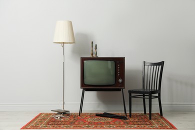 Photo of Retro TV on stand, black chair and lamp near white wall. Used stuff