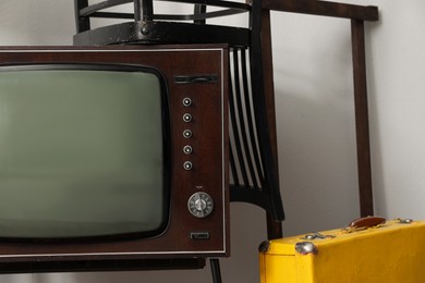 Photo of Retro TV, chairs and yellow suitacase near white wall. Used stuff