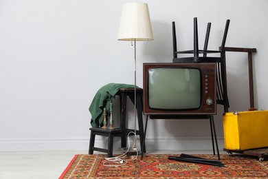 Photo of Retro TV on stand, black chair, suitcase and lamp near white wall, space for text. Used stuff
