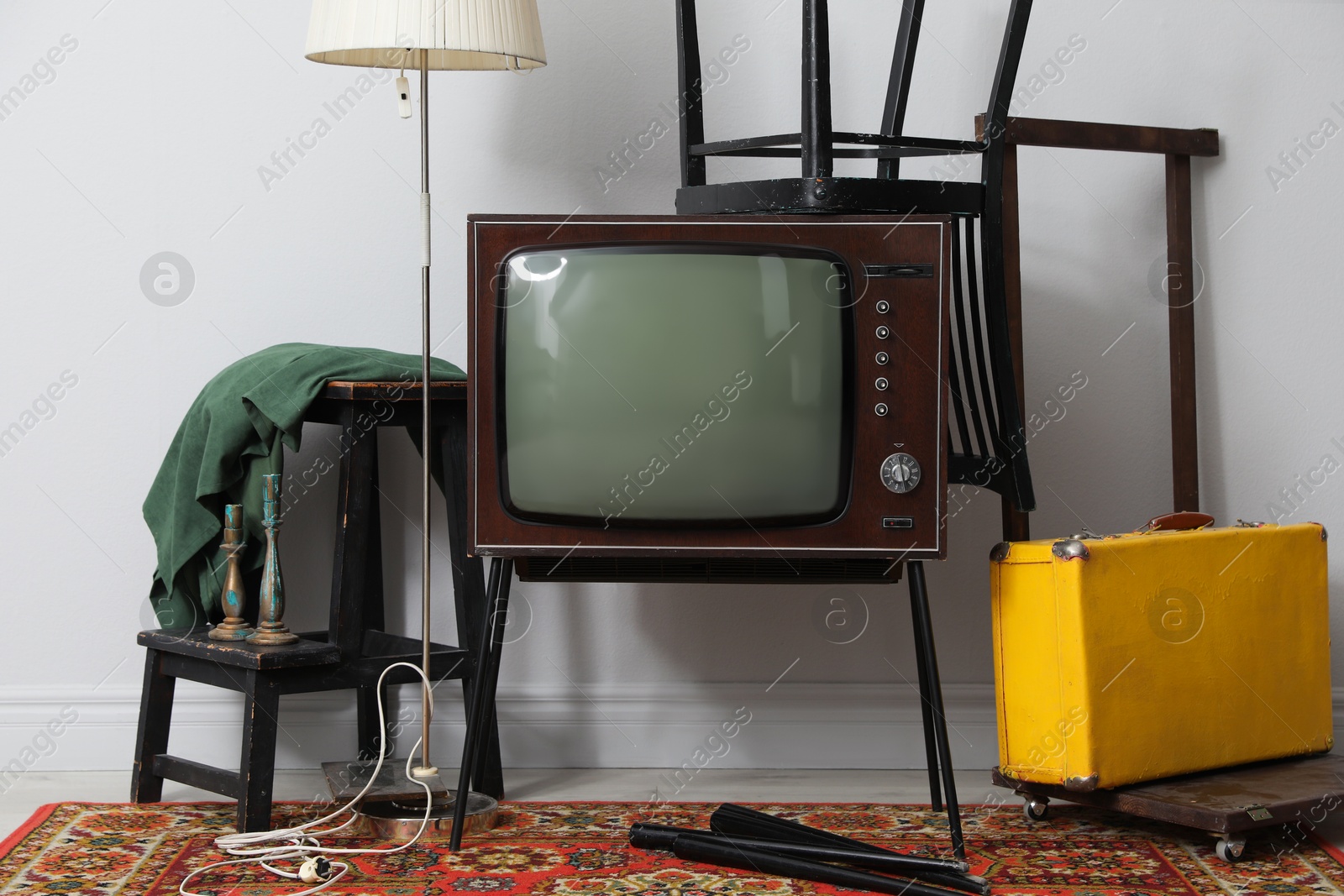Retro TV on stand, black chair, suitcase and lamp near white wall. Used stuff Photo of Retro TV on stand, black chair, suitcase and lamp near white wall. Used stuff