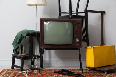 Photo of Retro TV on stand, black chair, suitcase and lamp near white wall. Used stuff