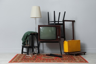 Photo of Retro TV on stand, black chair, suitcase and lamp near light grey wall. Used stuff