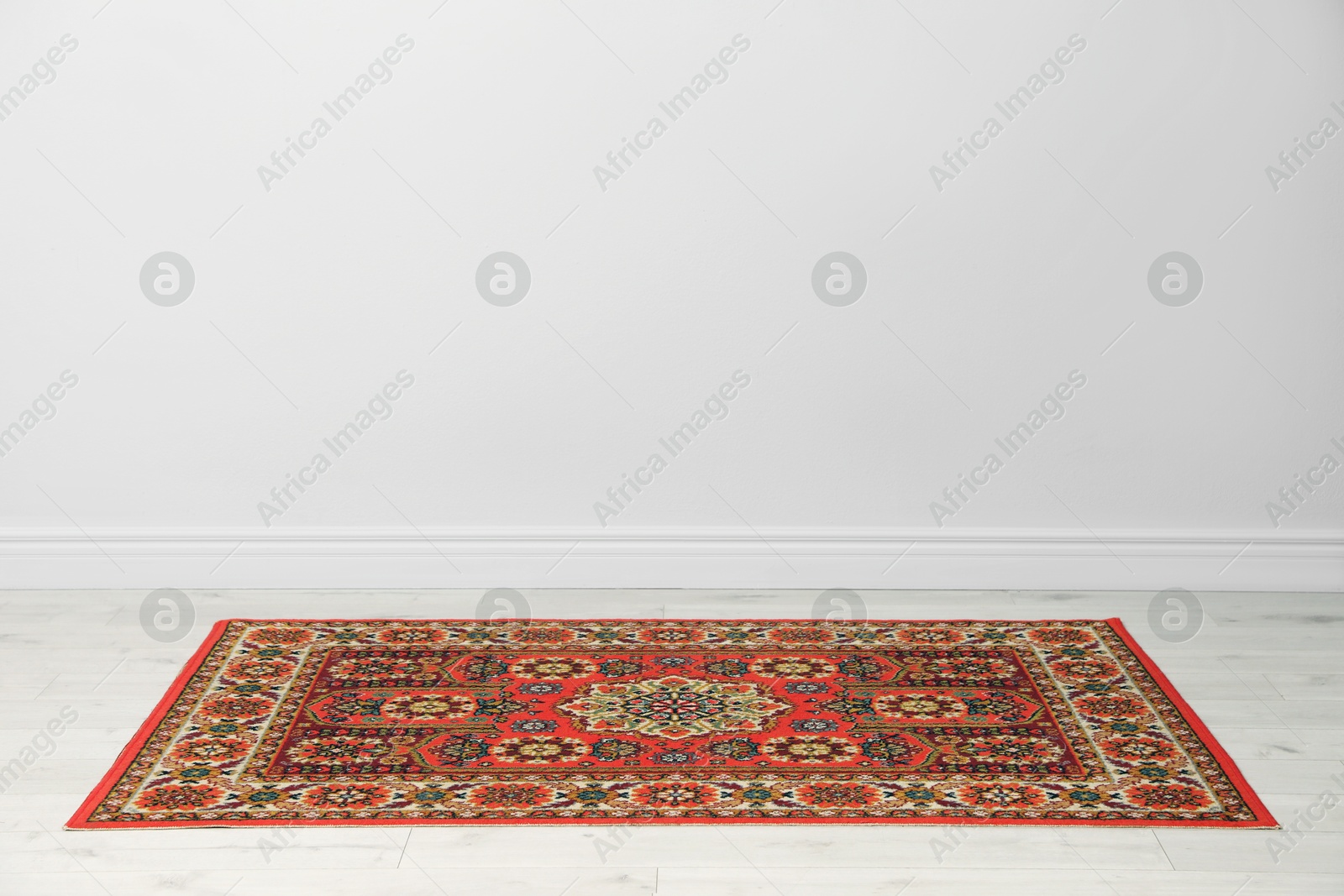 Soft red carpet with pattern on light wooden floor near white wall, space for text. Used stuff Photo of Soft red carpet with pattern on light wooden floor near white wall, space for text. Used stuff
