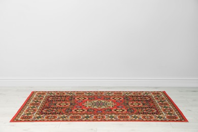 Photo of Soft red carpet with pattern on light wooden floor near white wall, space for text. Used stuff