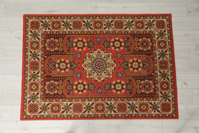Photo of Soft red carpet with pattern on light wooden floor, top view. Used stuff
