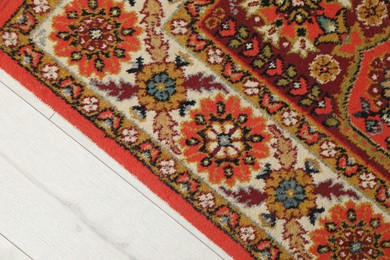 Photo of Soft red carpet with pattern on light wooden floor, top view. Used stuff