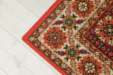 Photo of Soft red carpet with pattern on light wooden floor, top view. Used stuff