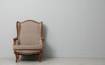 Photo of Old-fashioned armchair near light grey wall, space for text. Used stuff
