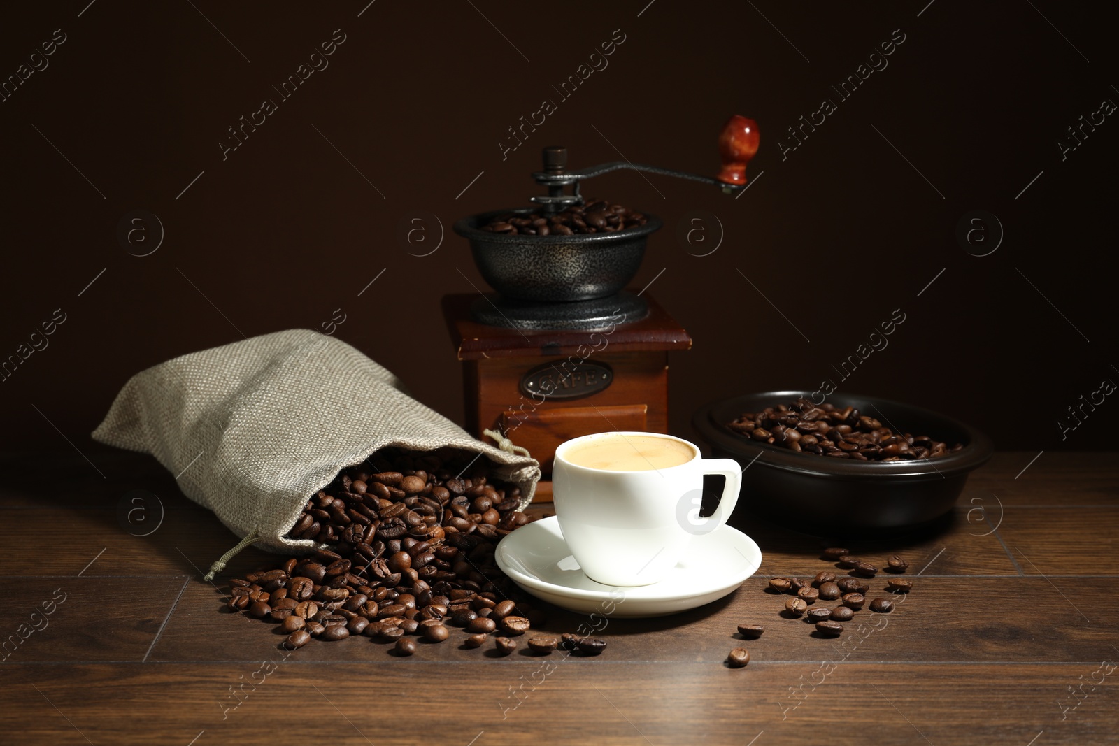 Aromatic coffee in cup, beans and grinder on wooden table against brown background Photo of Aromatic coffee in cup, beans and grinder on wooden table against brown background