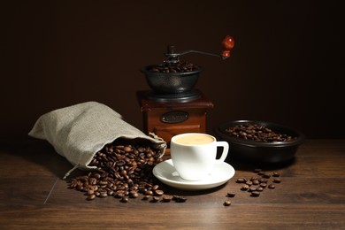Photo of Aromatic coffee in cup, beans and grinder on wooden table against brown background