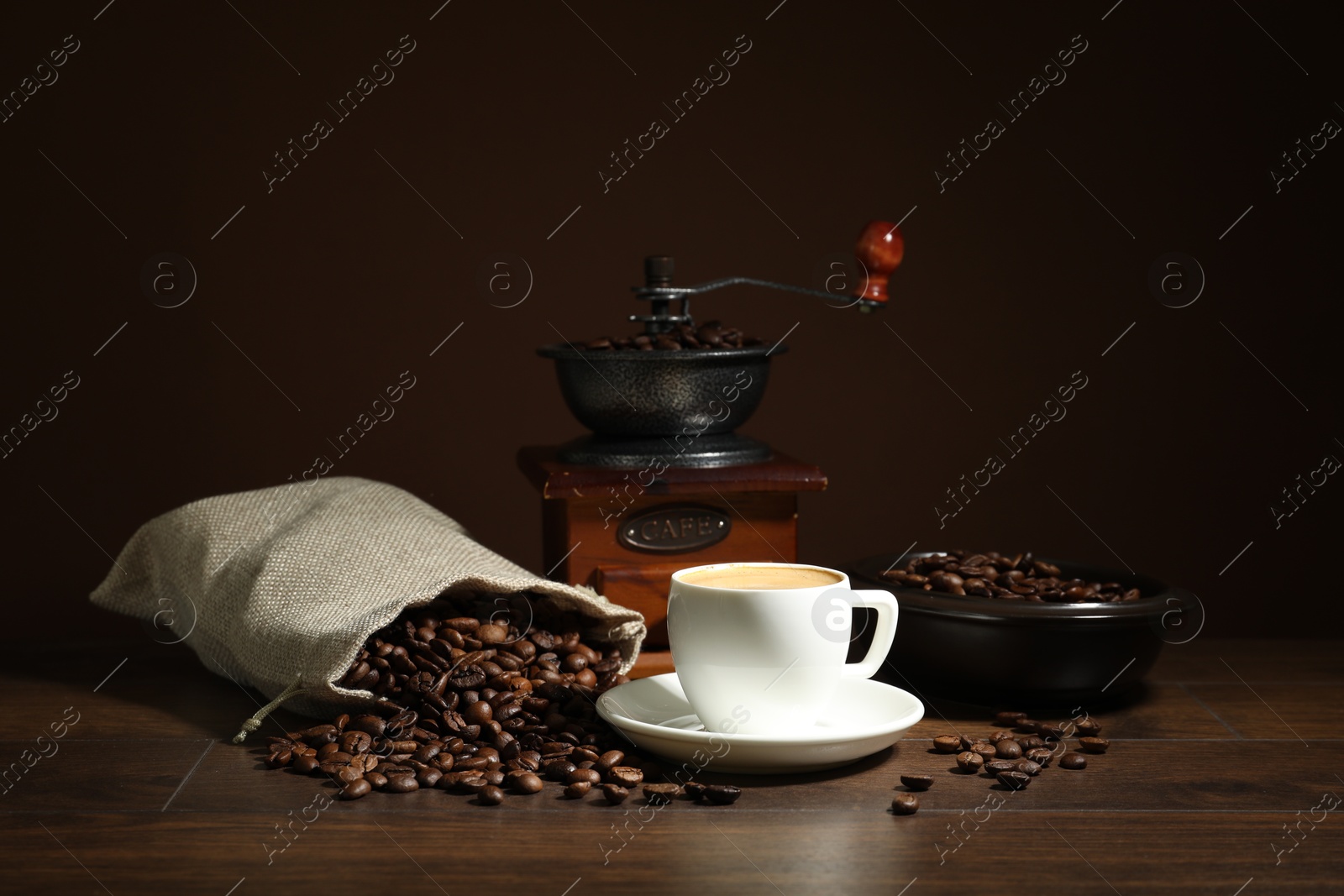 Photo of Aromatic coffee in cup, beans and grinder on wooden table against brown background