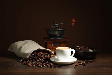 Photo of Aromatic coffee in cup, beans and grinder on wooden table against brown background