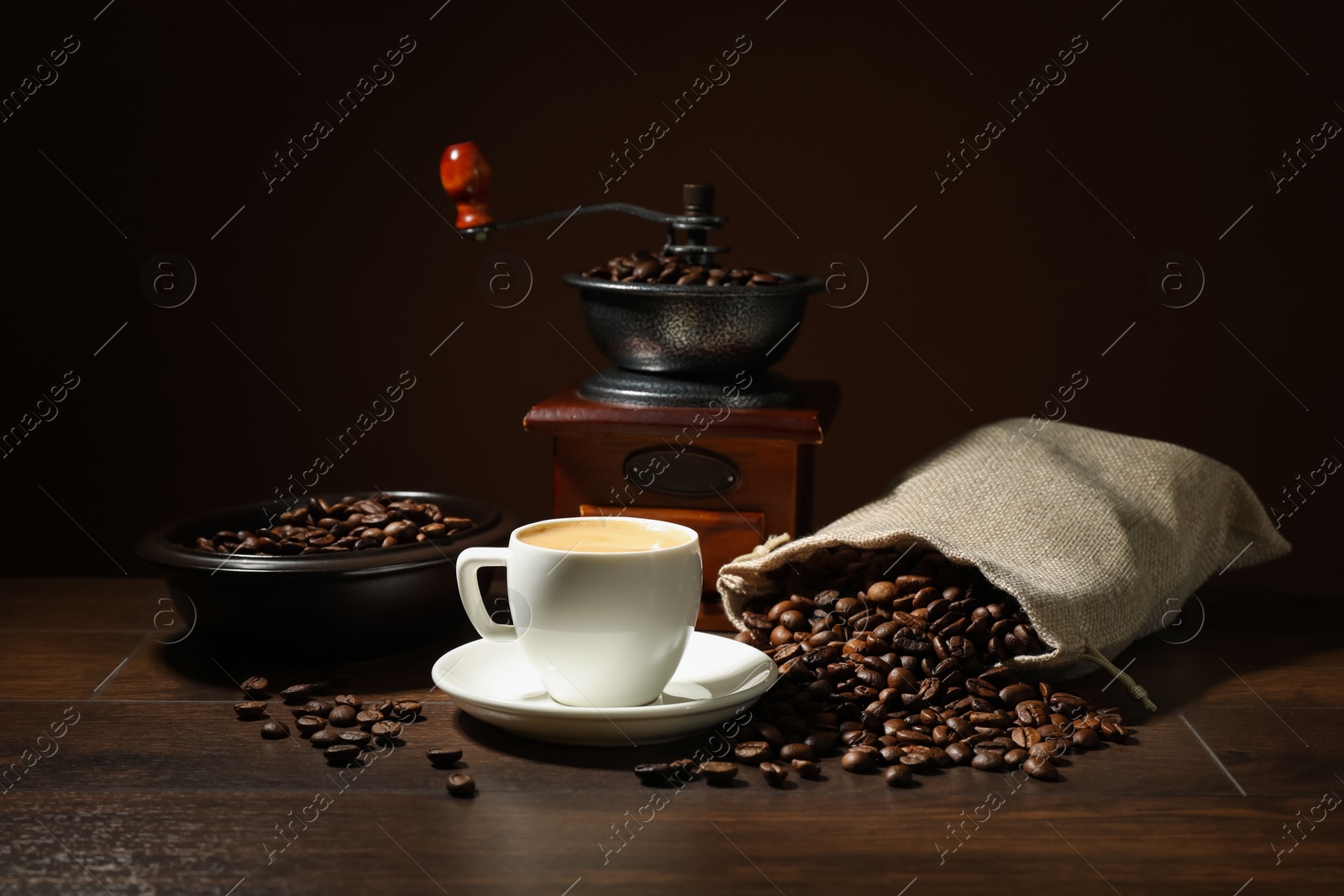 Aromatic coffee in cup, beans and grinder on wooden table against brown background Photo of Aromatic coffee in cup, beans and grinder on wooden table against brown background