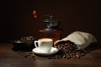 Photo of Aromatic coffee in cup, beans and grinder on wooden table against brown background