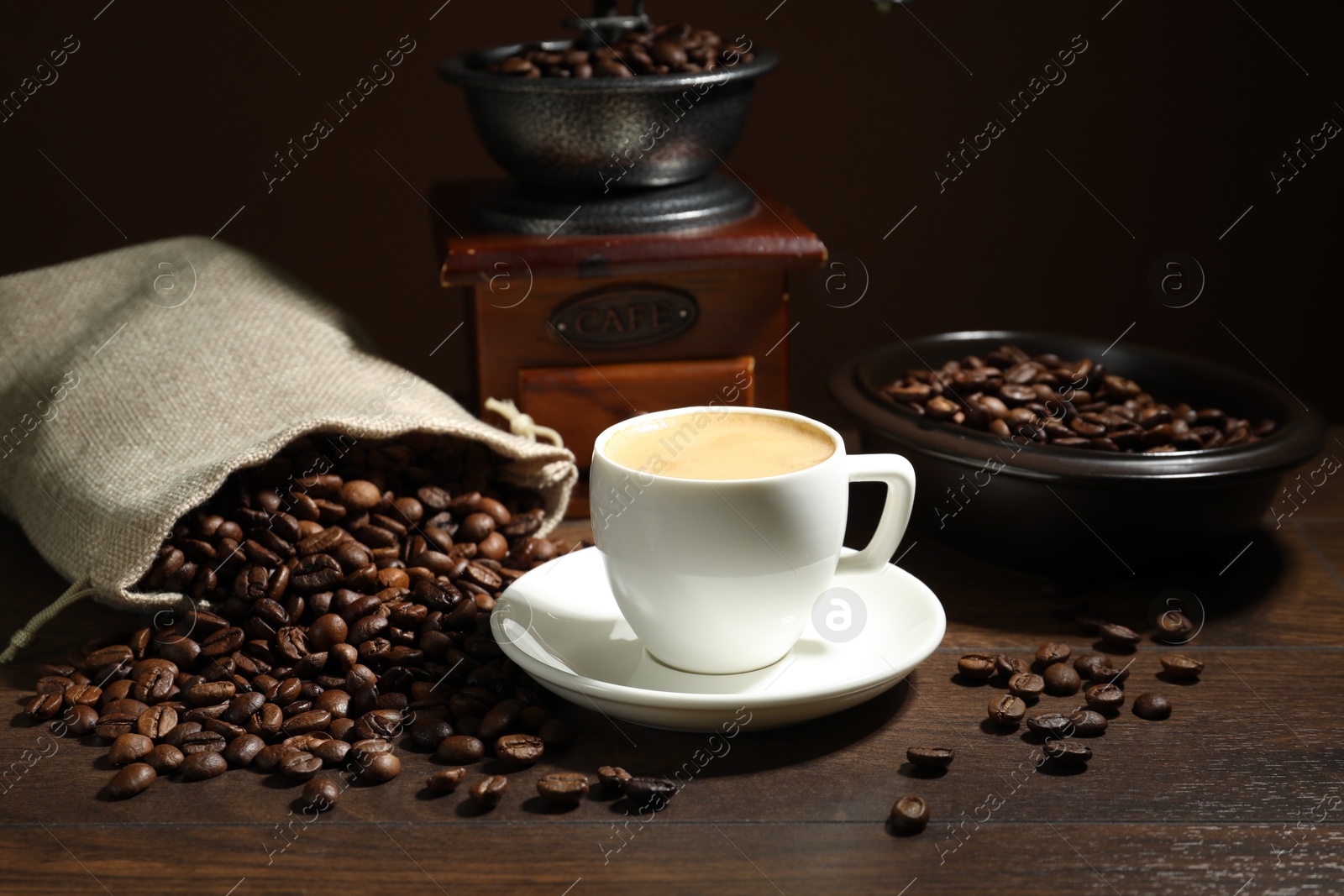Aromatic coffee in cup, beans and grinder on wooden table against brown background Photo of Aromatic coffee in cup, beans and grinder on wooden table against brown background