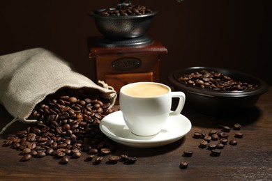 Photo of Aromatic coffee in cup, beans and grinder on wooden table against brown background