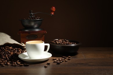 Photo of Aromatic coffee in cup, beans and grinder on wooden table against brown background, space for text
