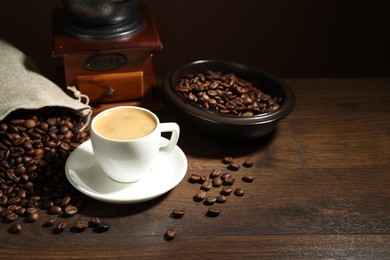Photo of Aromatic coffee in cup, beans and grinder on wooden table, space for text